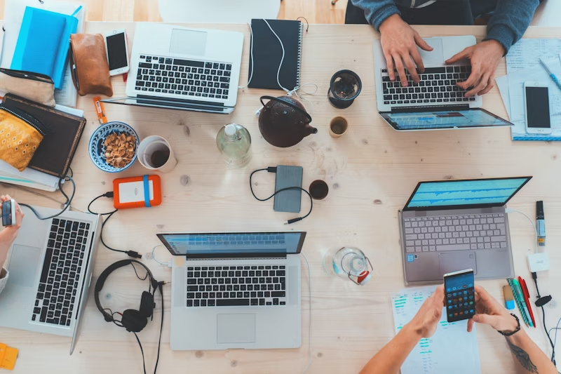 Mesa de trabajo con múltiples laptops, teléfonos móviles y accesorios de oficina, representando un entorno colaborativo para la automatización de redes sociales y soluciones de IA.